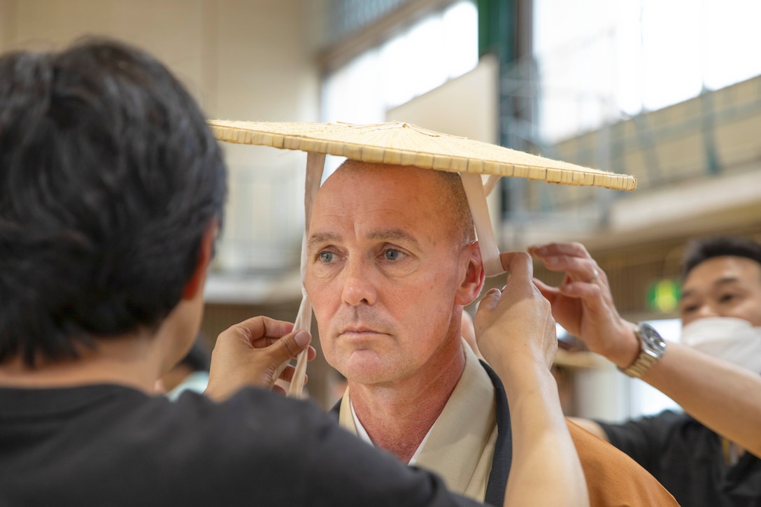 A close-up of two people putting a Japanese hat on a Marine.