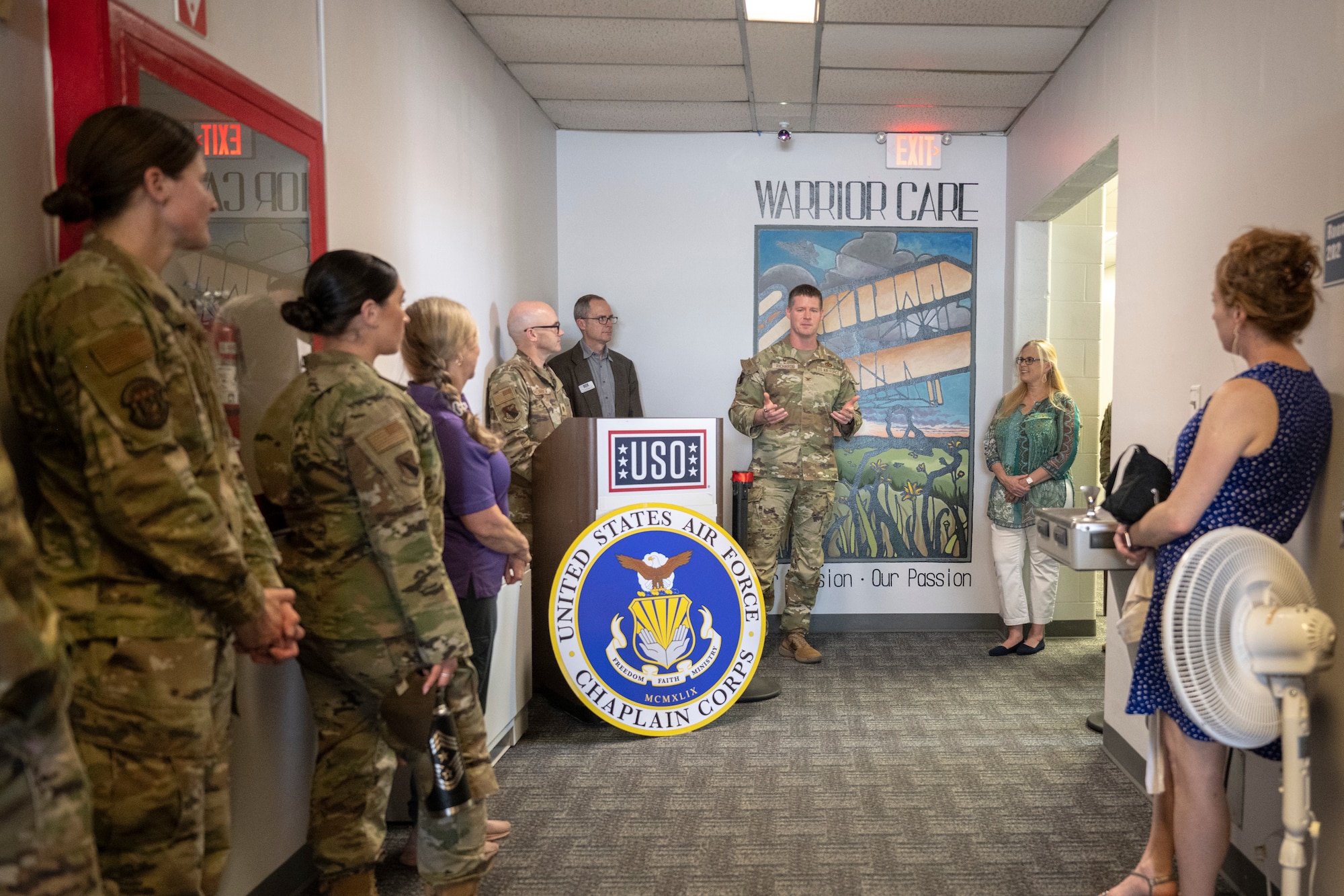 Col speaks to attendees during a ceremony. Mural in the background.