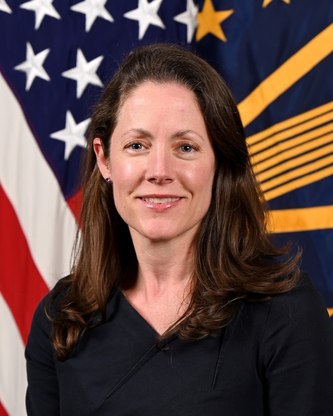 A woman poses for an official photo in front of flags.