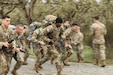 A group of soldiers sprint while wearing backpacks and holding rifles.