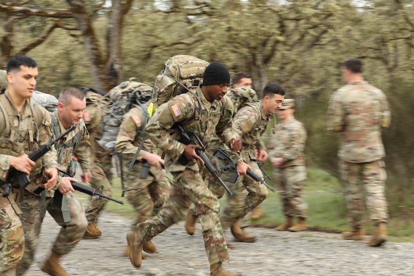 A group of soldiers sprint while wearing backpacks and holding rifles.