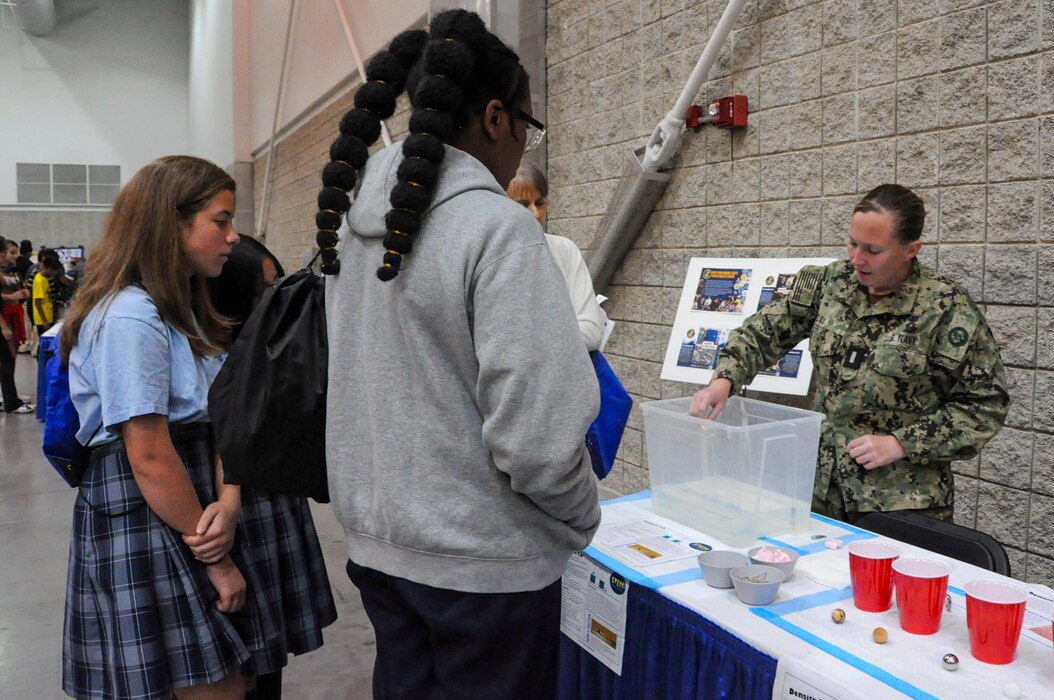 Navy and Marine Corps Force Health Protection Command (NMCFHPC) participated in the Joint Base Langley-Eustis (JBLE) and Armed Forces Communications and Electronics Association International (AFCEA) Tidewater Chapter, Science Technology Engineering and Mathematics (STEM) day at the Tidewater Integrated Combat Symposium (TWICS) May 8, 2024. The event, held at the Hampton Roads Convention Center, in Hampton, Virginia, was aimed at providing students with hands-on interactions and expose them to potential career pathways. NMCFHPC staff established a booth to educate the students about gravity and buoyancy, as well as robotics, computer programming, and cybersecurity. NMCFHPC staff established a booth to educate the students about gravity and buoyancy, as well as robotics, computer programming, and cybersecurity. During the event, Lt. j. g. Kerry Day, an environmental health officer at the Navy and Marine Corps Force Health Protection Command, performs a demonstration at the Flinkers station for the students. The Flinkers experiment measures the buoyancy of the objects that the students construct and place into the water. According to the Archimedes Principle, an object partially or fully emerged in a fluid will experience a resultant force pushing up on it equal to the weight of the volume of fluid displaced by the object. This vertical force is called the force of buoyancy. The buoyant force on an object is equal to the weight of the volume of water displaced by the object. When the weight of the object submerged is equal to the upward buoyant force exerted by the water, the object is neutrally buoyant, so it doesn’t sink or float, it flinks. (Navy photo by Desmond Martin)