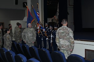 Airmen stand in attention in front of honor guard members holding the flags.