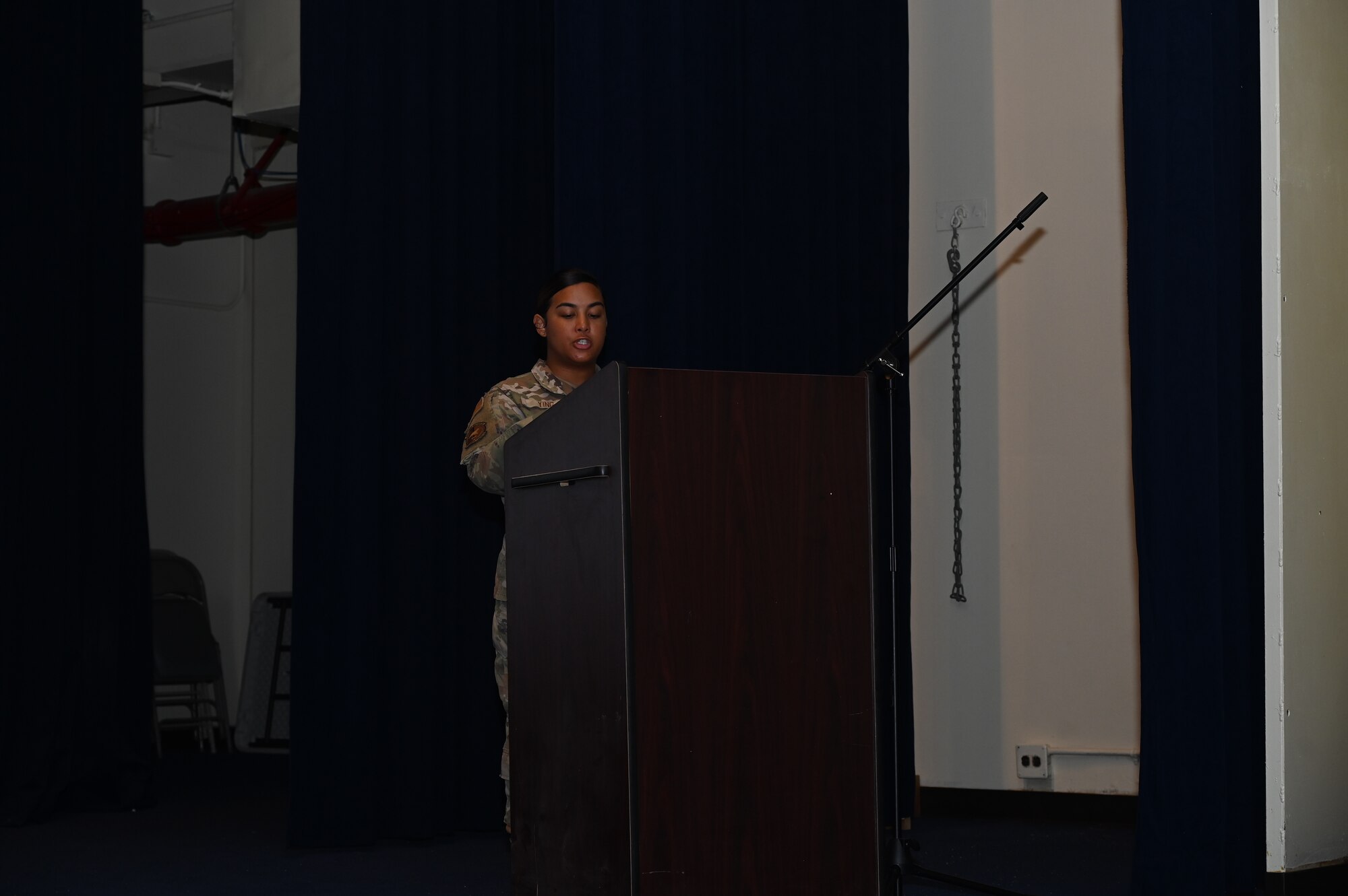 An Airman stands on the stage behind a podium and reads the Security Forces prayer.