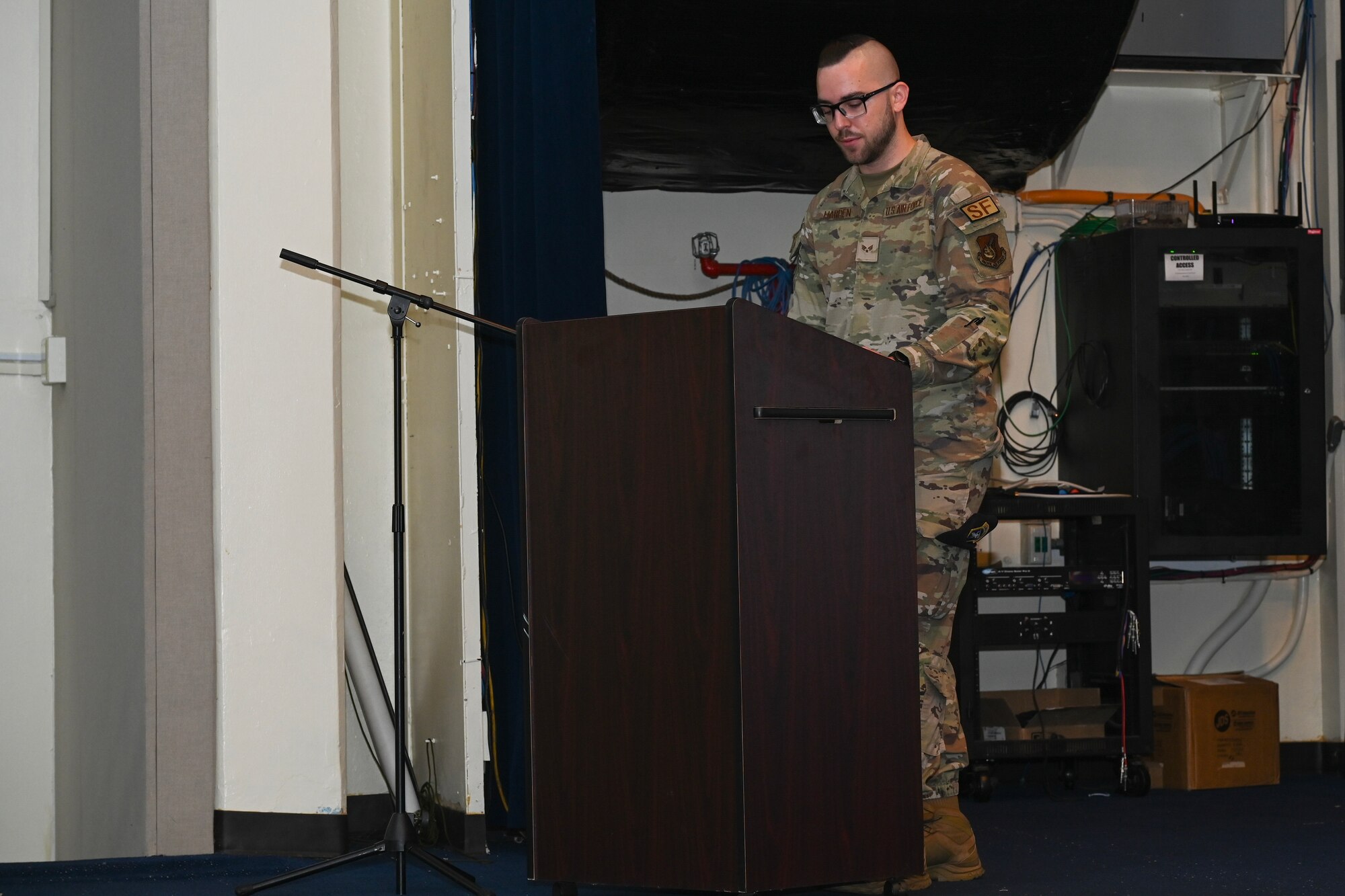 An Airman stands behind a podium on stage and reads to the audience the history of Police Week.