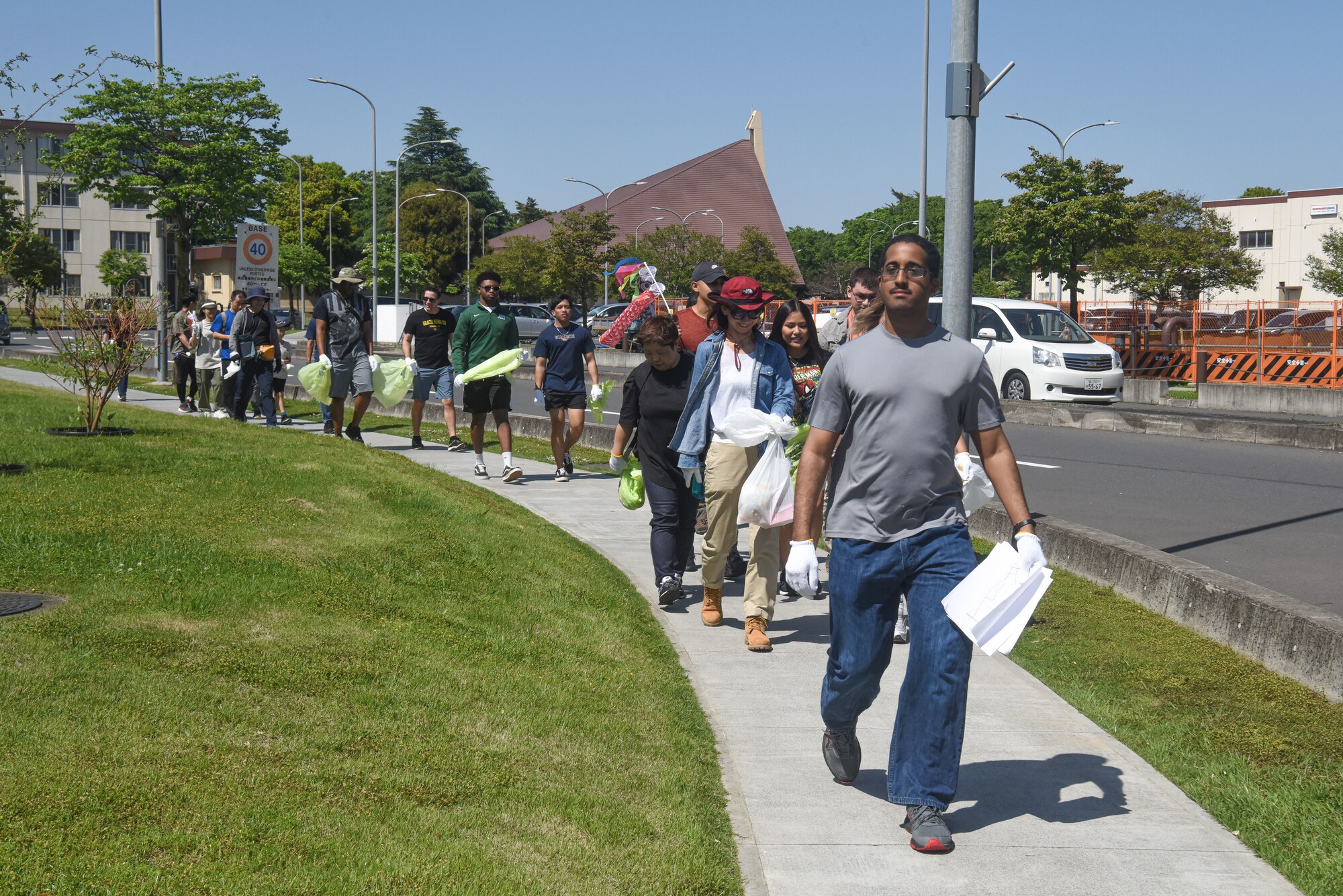 Group of participants with garbage bags walk in a single-file line down the sidewalk.