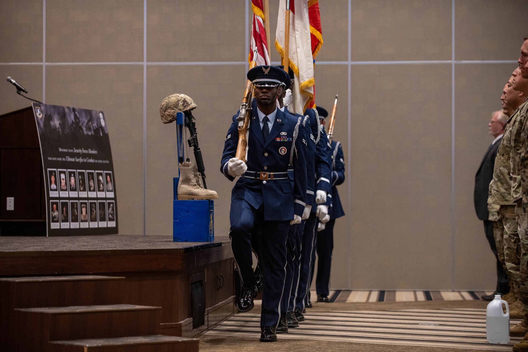 military members holding flags march in step at the front of a stage