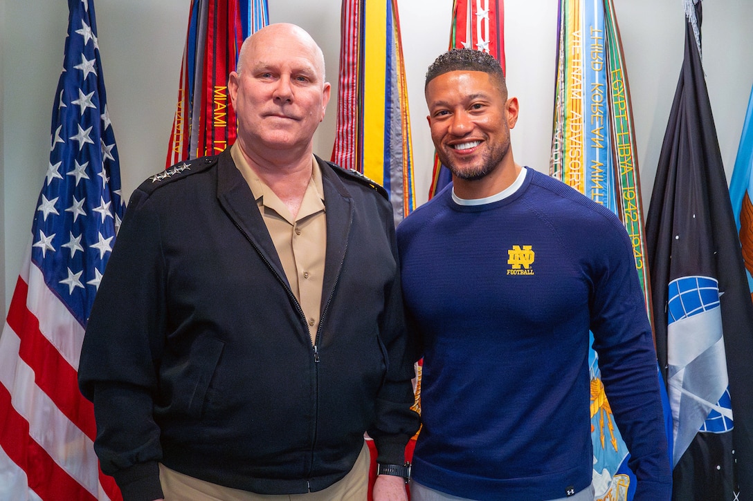 Navy Adm. Christopher W. Grady, vice chairman of the Joint Chiefs of Staff, stands with a civilian in front of a row of flags.