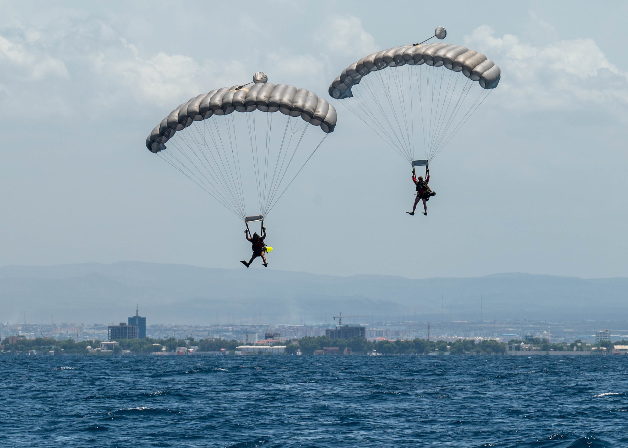 Two U.S. servicemembers parachute above water.