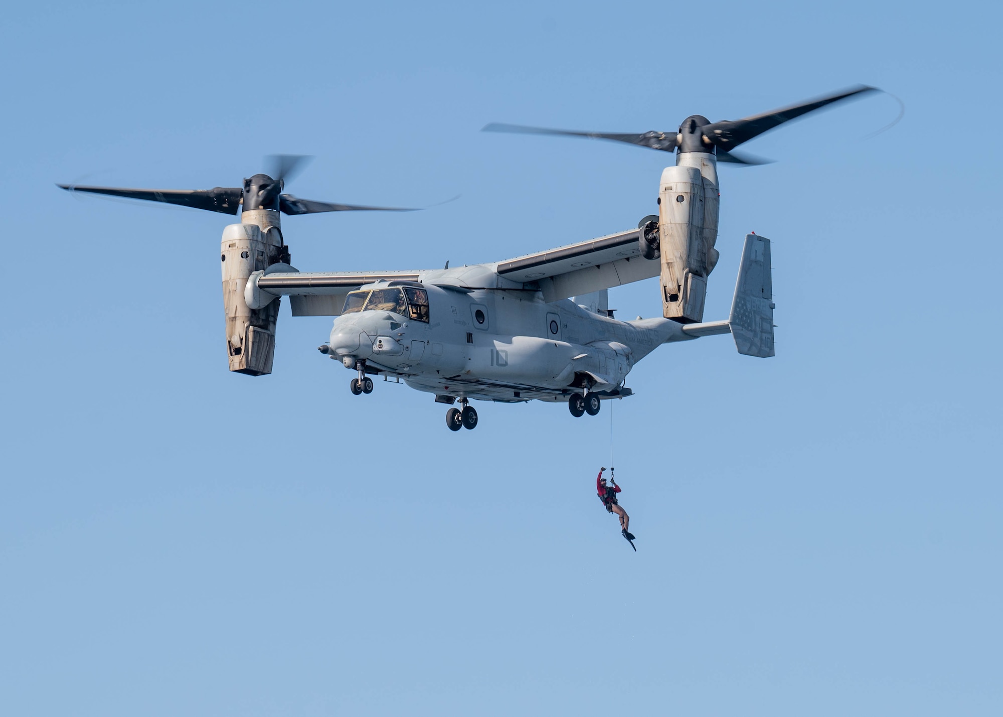 A person repels down from a tiltrotor aircraft during a military training exercise