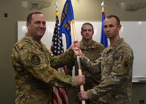 Major Bryan Ashton accepts a blue flag with gold letters from Lieutenant Colonel Cas Smith during a ceremony May 13, 2024, representing Ashton taking command of the 582nd Operations Support Squadron's Detachment 1 at Malmstrom Air Force Base, Montana.