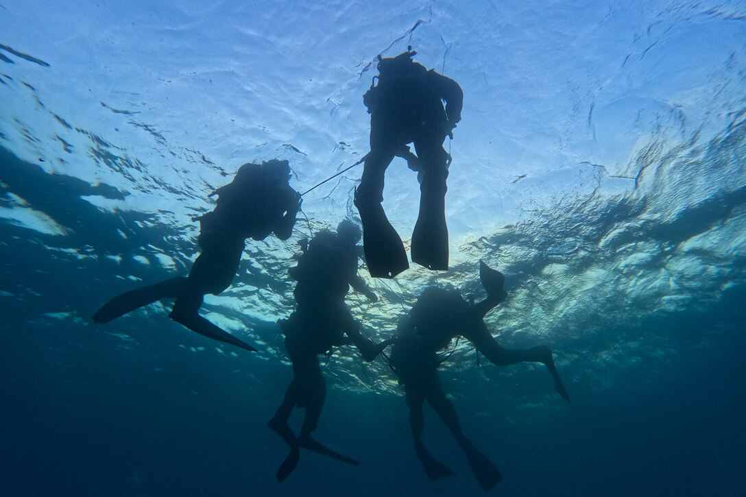 Six Marine Corps divers are photographed from below while underwater.