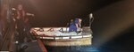 A US Coast Guard boat crew member boards a migrant vessel with spotlight shone on it.