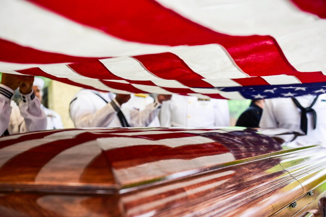 A close-up of a sailors’ hands holding an American over a casket.