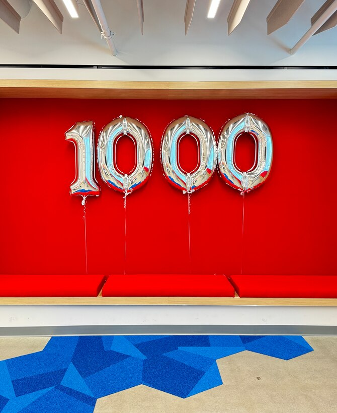 Silver balloons reading 1000 against a bright red backdrop