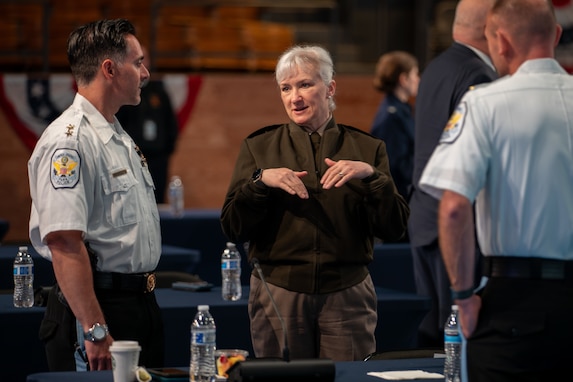 An Army soldier in green service uniform is gesturing with her hands while talking with first responders during a break in a meeting.