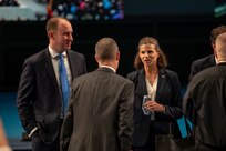Several people in business attire are standing in a large room talking with each other.