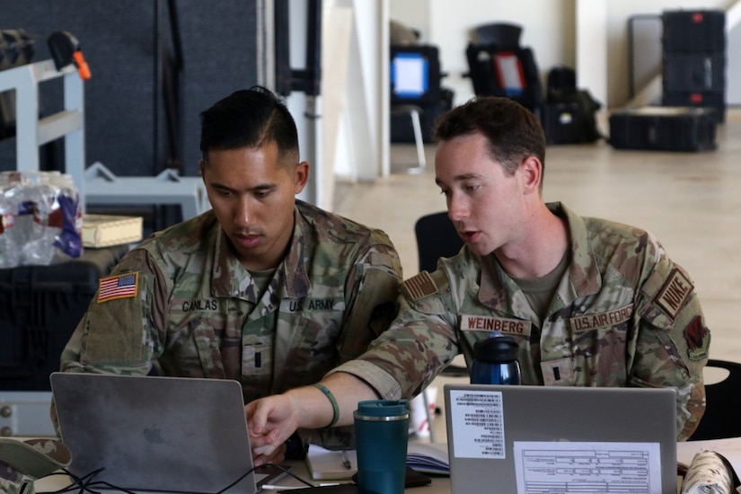 Two soldiers work on laptops while sitting at a table.