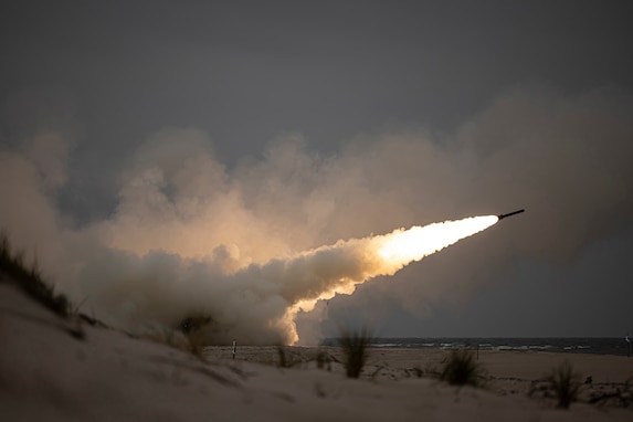 A rocket is fired over a beach at night leaving a fiery tail in its wake.