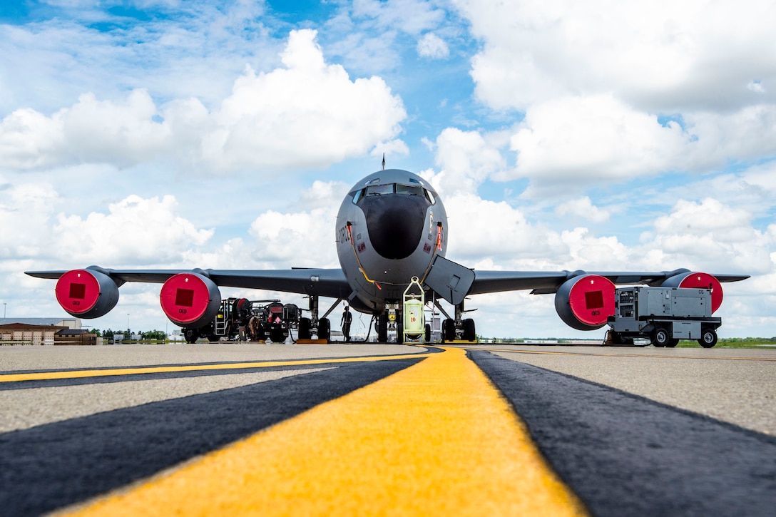 A large aircraft sits on a flight line with airmen and vehicles around it.