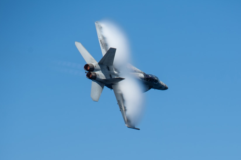 A jet flies leaving vapor against a blue sky.