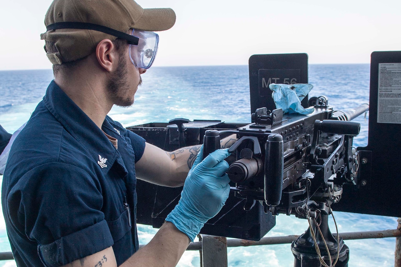 A sailor maintains a gun on a ship.