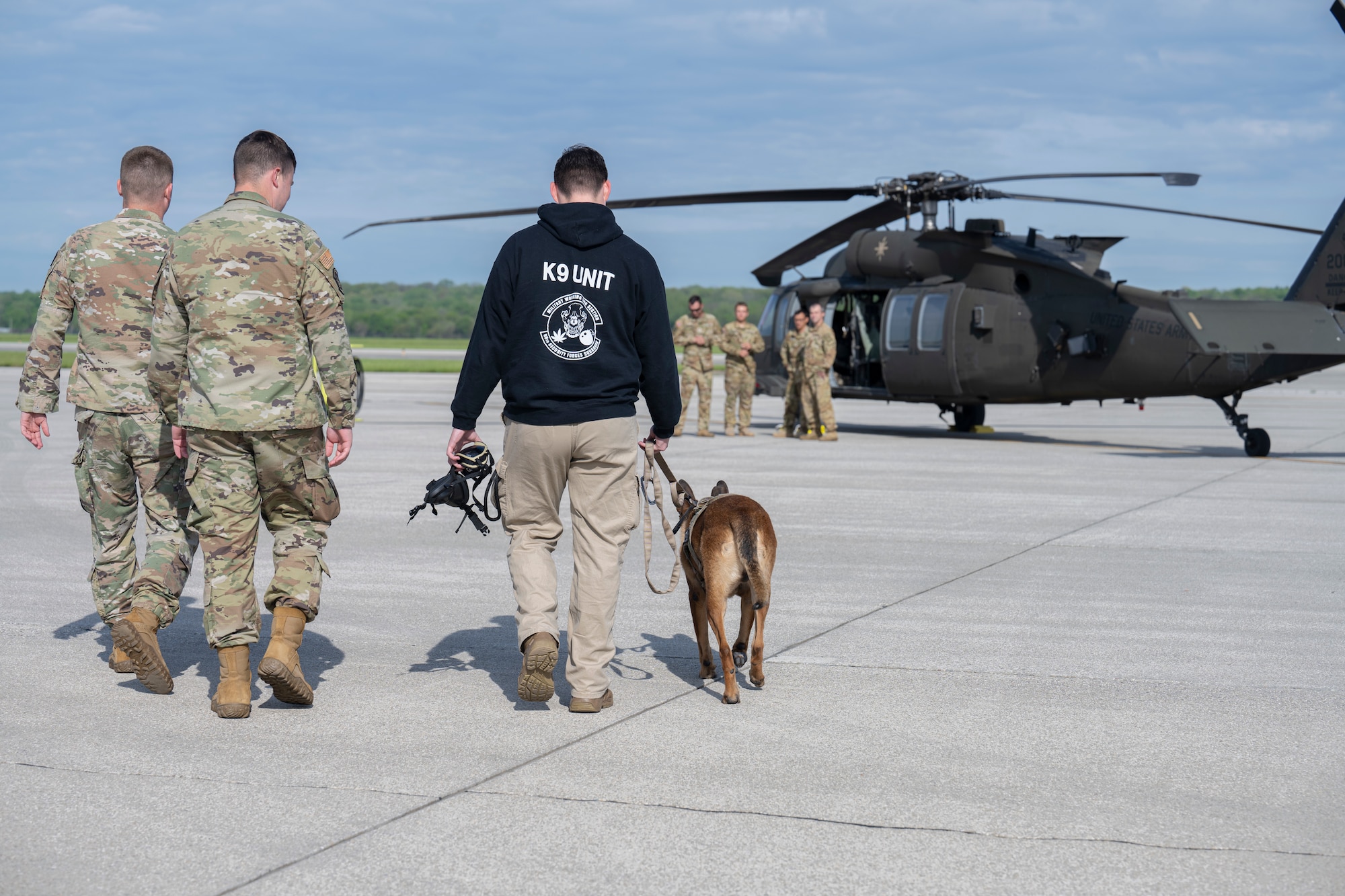 Two uniformed Airmen and MWD handler and MWD walk toward aircrafts on the flightline.