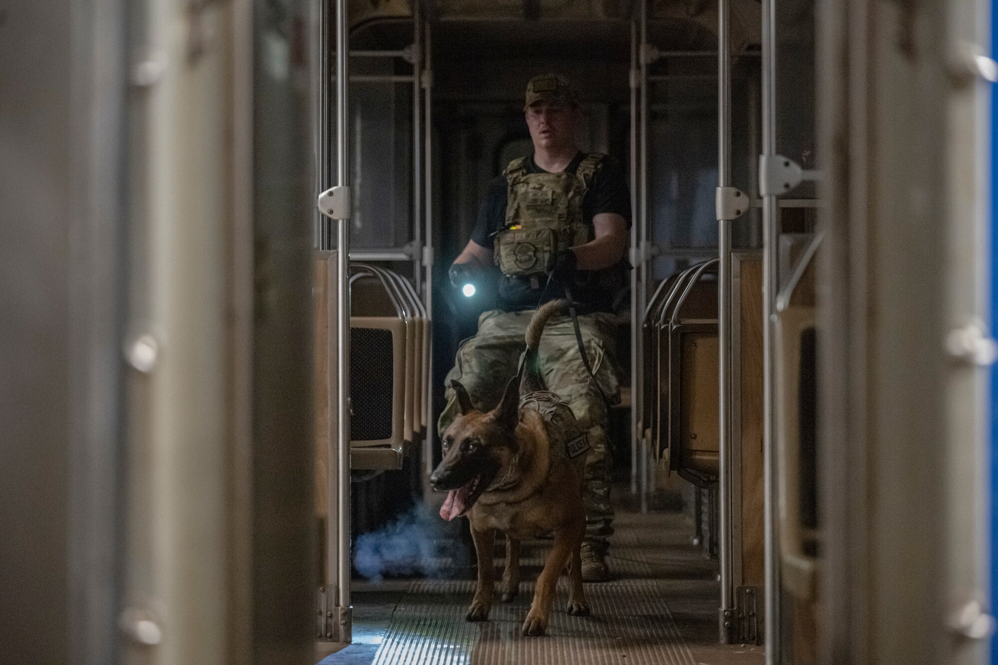 MWD handler and K9 inside a rapid transit system. Handler holds flash light.