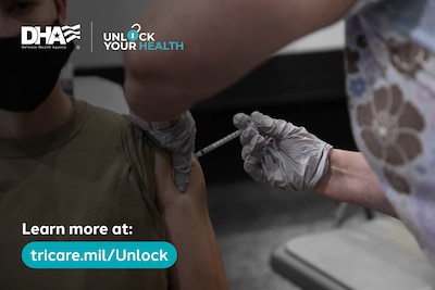 A gloved hand injects a vaccine into the upper arm of a service member.