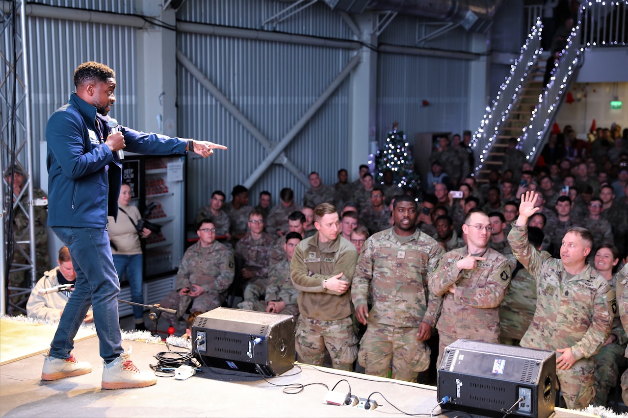 A man on stage points at a man in the front row of an audience, who puts up his hand in response.