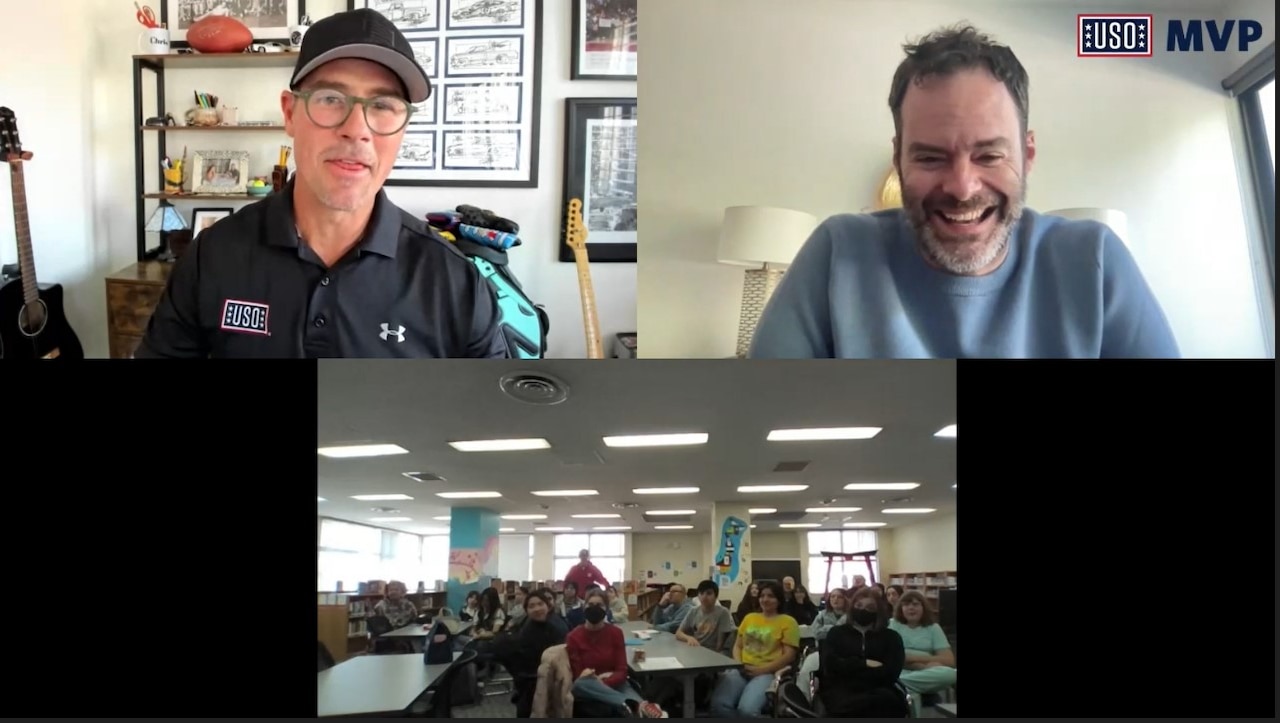 Two screens show two men smiling and laughing. A third screen shows a classroom full of teenagers.