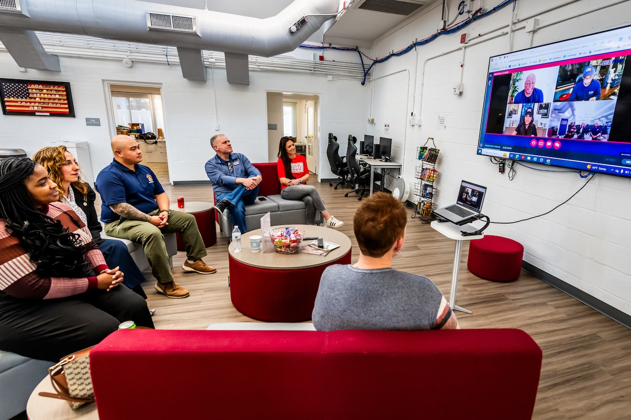 Several people sitting in plush chairs watch the same TV.
