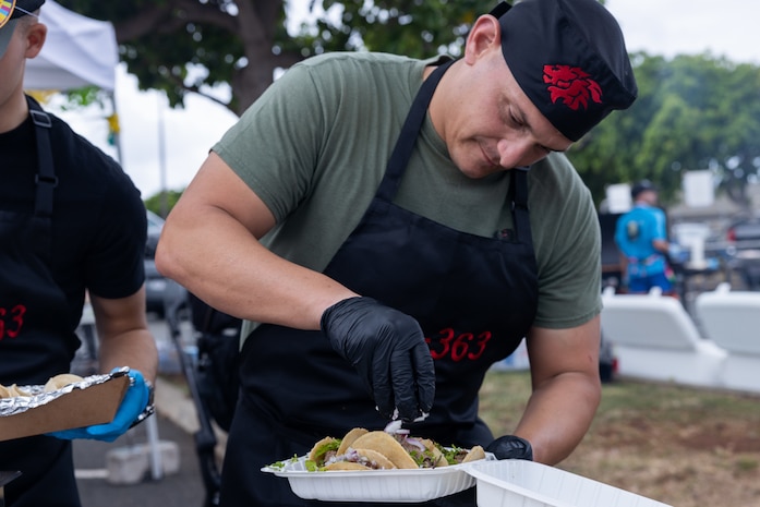 A U.S. Marine with Marine Medium Tiltrotor Squadron (VMM) 363, Marine Aircraft Group 24, 1st Marine Aircraft Wing, prepares tacos for a customer during the 2024 Tacolympics, a cooking and fundraising event, Marine Corps Base Hawaii, May 3, 2024. The contest provided MCBH units an opportunity to compete and raise funds towards their unit Marine Corps Birthday Balls, while celebrating Hispanic culture and diversity. (U.S. Marine Corps photo by Lance Cpl. Tania Guerrero)
