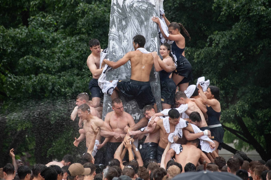 U.S. Naval Academy freshmen try to climb a stone monument covered with grease.