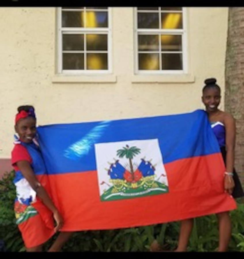 U.S. Marines Sgt. Mehdrina Jeancharles (left) and Sgt. Sophie Jeancharles pose with a Haitian flag during their childhood, in front of their home in Florida. The Jeancharles sisters are twins born in Saint Marc, Haiti and raised in West Palm Beach Fl. Surviving a series of unfortunate events such as natural disasters, the twins moved to the US as teenagers eventually becoming non-commissioned officers in the U.S. Marine Corps. (Courtesy photo provided by U.S. Marine Corps Cpl. Mehdrina Jeancharles)