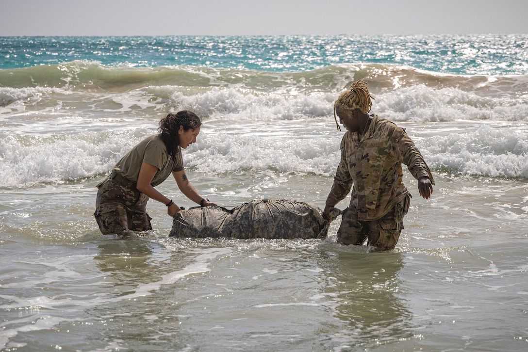 Two soldiers pull a ruck toward the shore during training.