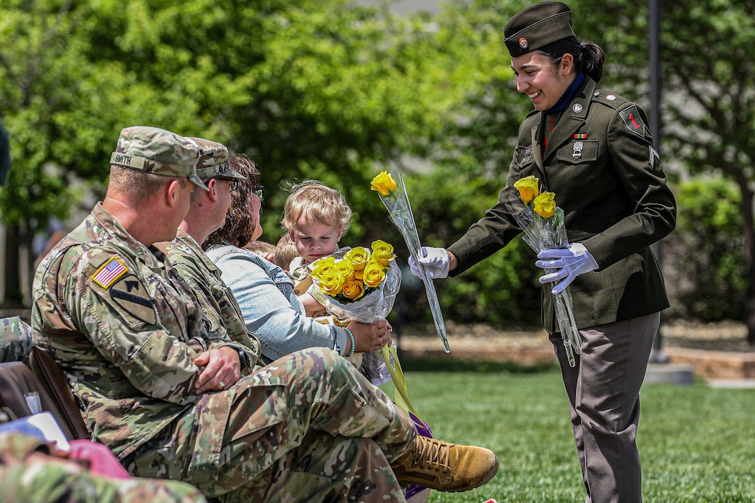 A soldier hands a yellow flower to a seated military spouse as others watch.