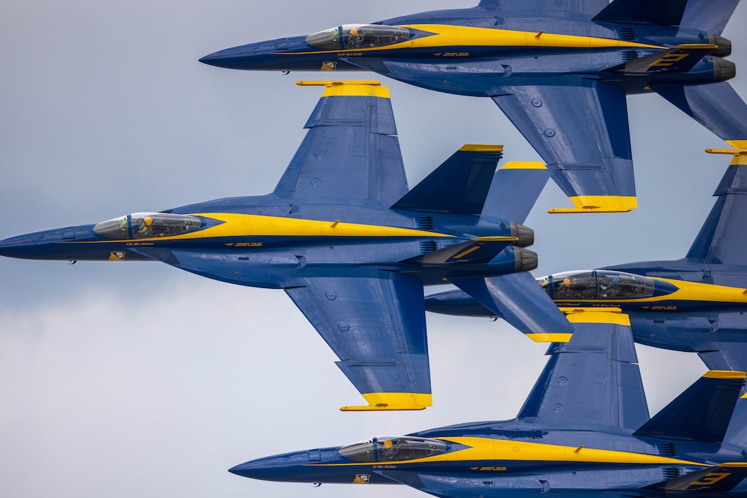 Four blue military aircraft with yellow accents fly close together in a diamond formation.