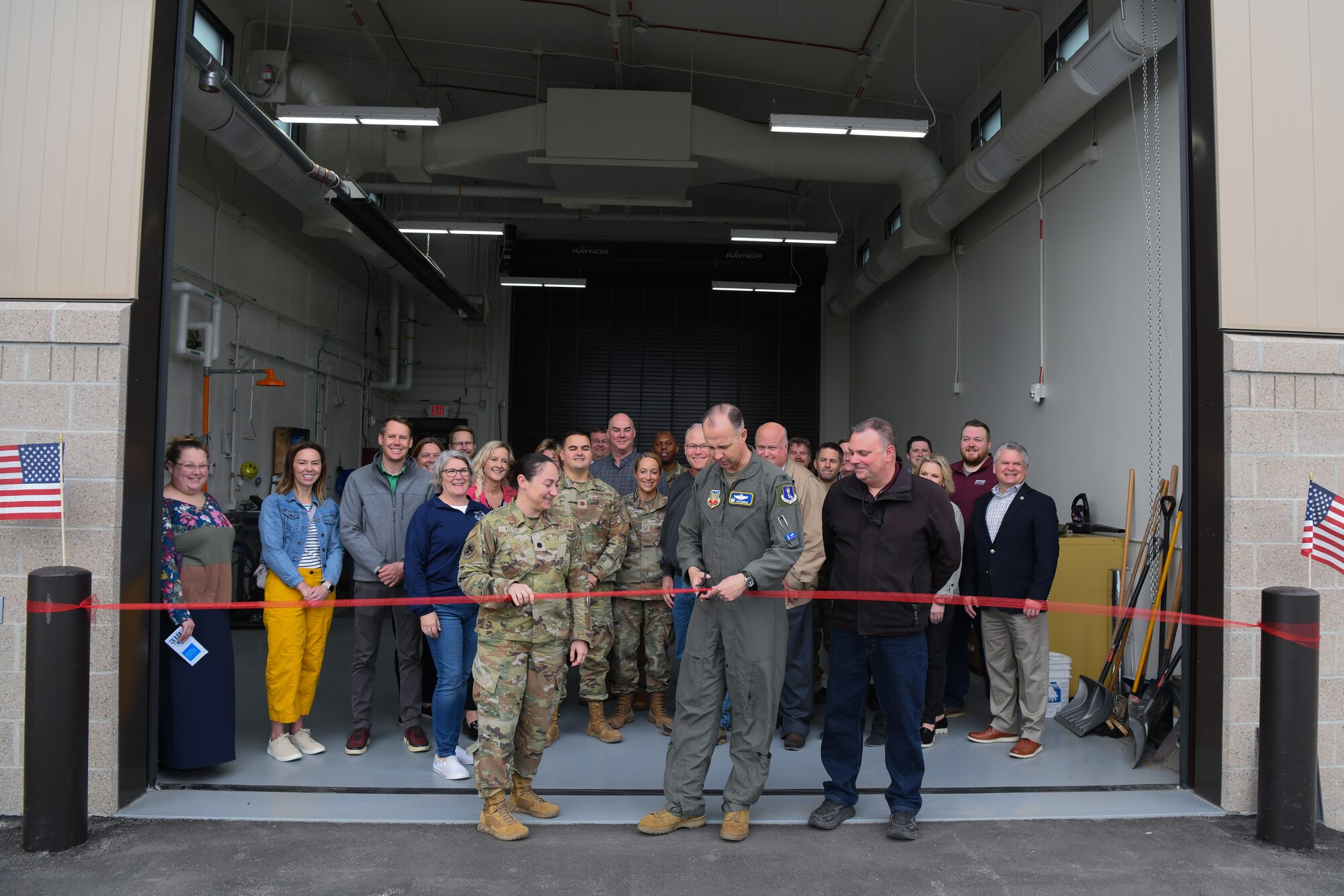 Military members and civilians pose for a photo will cutting a ribbon on a newly opened building.
