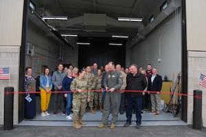 Military members and civilians pose for a photo will cutting a ribbon on a newly opened building.