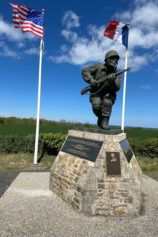 A statue of a service member holding a weapon. Two flags are in the background.