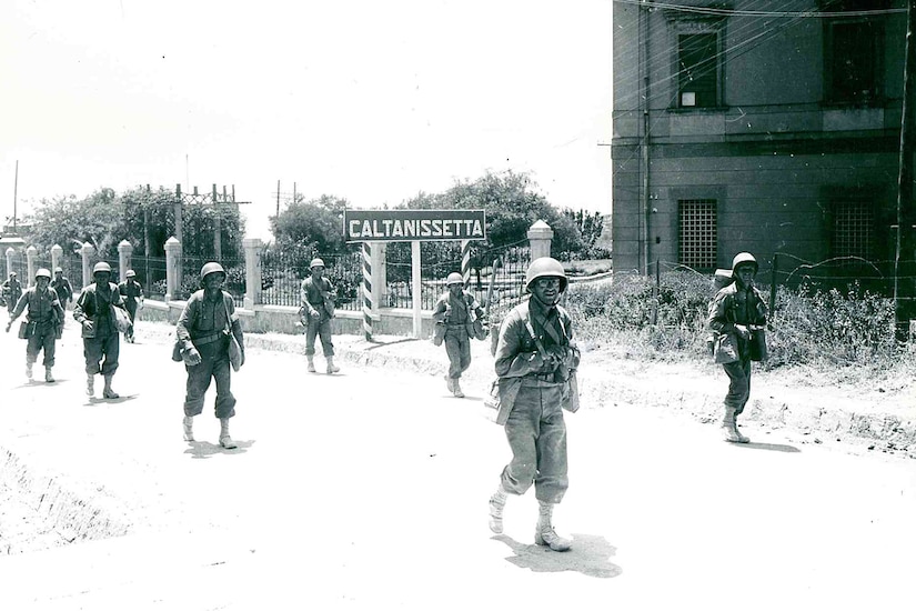 Men in formation walk along a roadway.