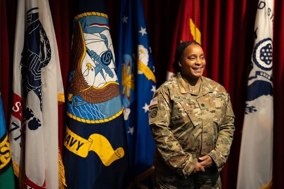 U.S. Army Soldier poses in front of flags at her promotion ceremony
