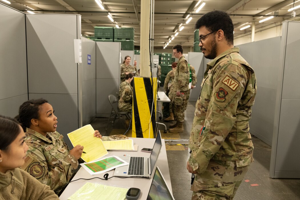 A Master Sergeant explains a form to an Airman in a processing line.