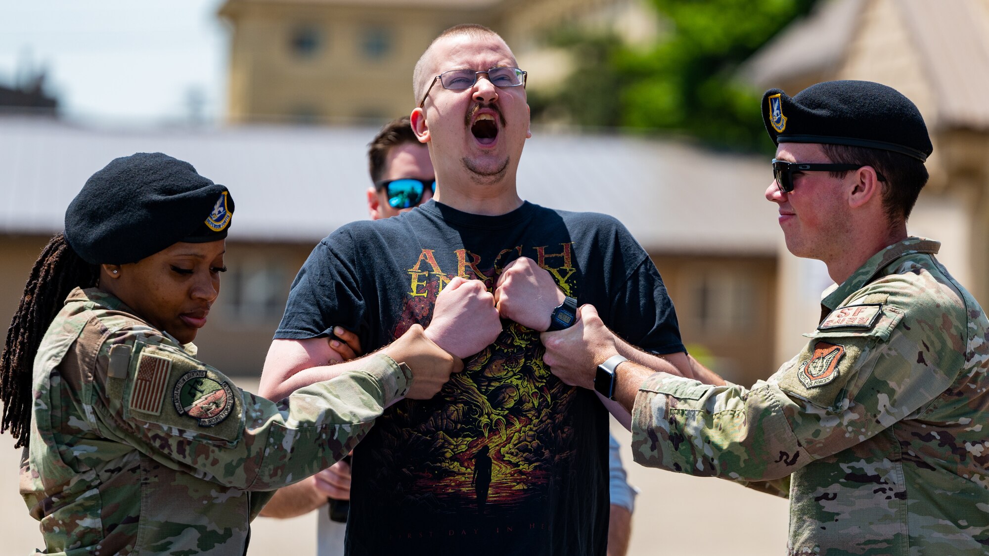 Senior Airman Cerona Green and Airmen 1st Class Parker Farnham brace Senior Airman Jesse Ross during a taser demonstration.