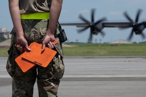 A marrshaller holding flags before directing a C-130J Super Hercules.