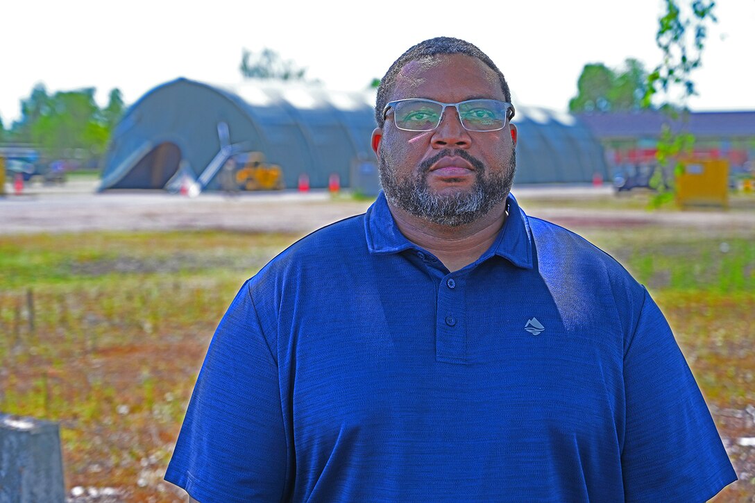 A man poses in a field with a large tent in the background.