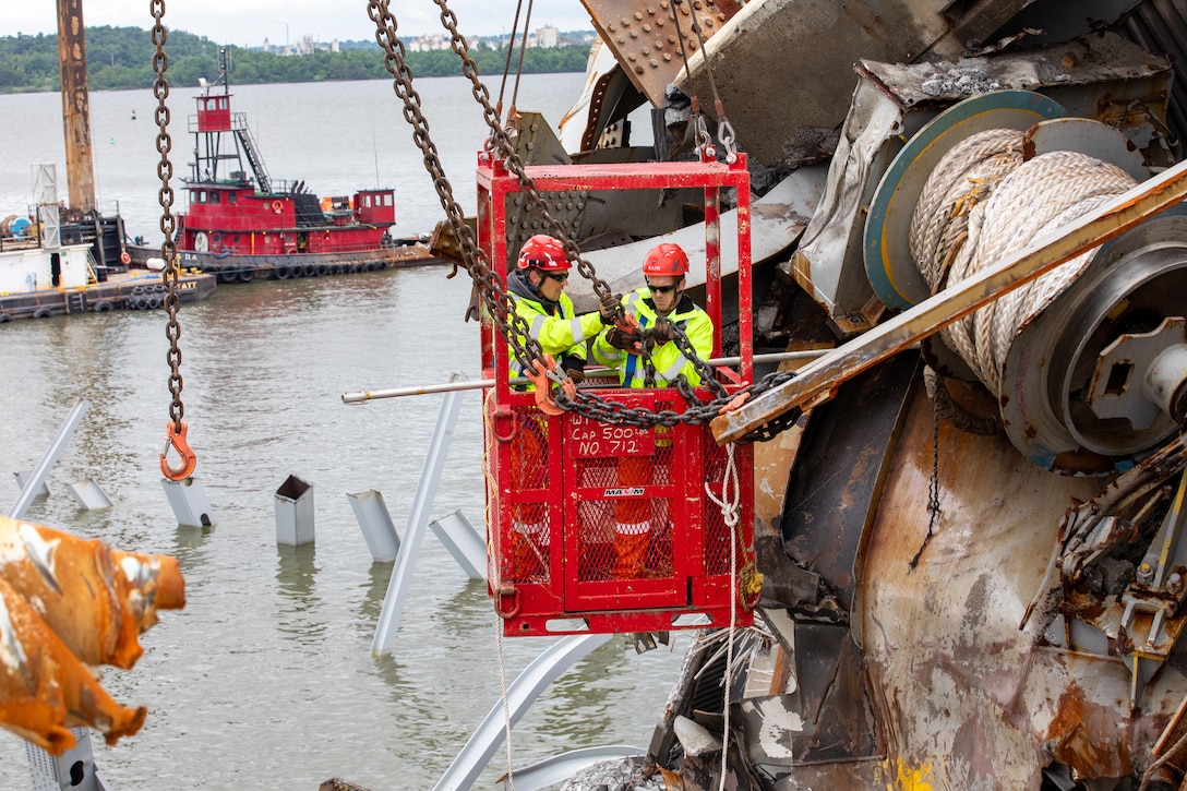 Two salvors work from a cherry picker to remove a mountain of debris from atop a ship in the wake of a bridge collapse.