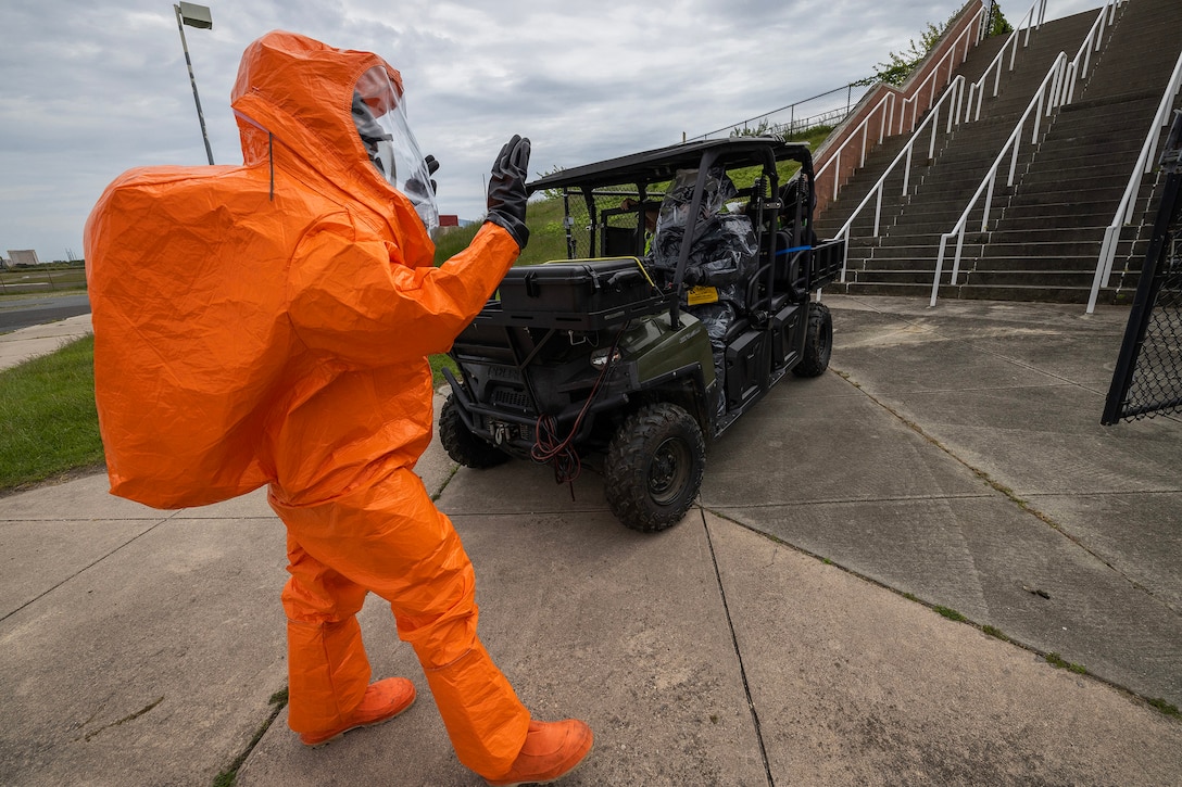 A service member in an orange hazmat suit gestures during training.