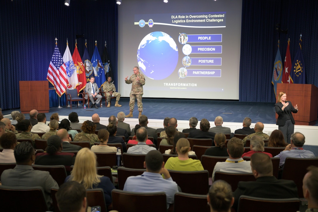 Lt. Gen Mark Simerly is onstage with a slide behind him describing people, precision, posture and partnership as he addresses an auditorium full of people